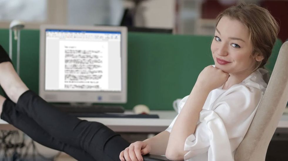 Kvinna med fötterna på skrivbordet, Word på dator i bakgrunden